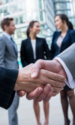 Two business people shaking hands with a blurred office building in the background